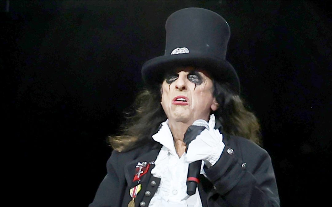 Alice Cooper wearing a black top hat and holding a microphone onstage.